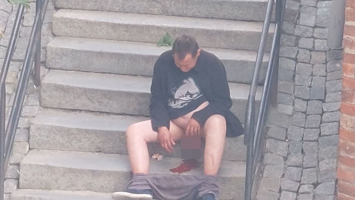 Bezdomny zakrawiony, bez spodni, siedzi na schodkach w Oleśnicy